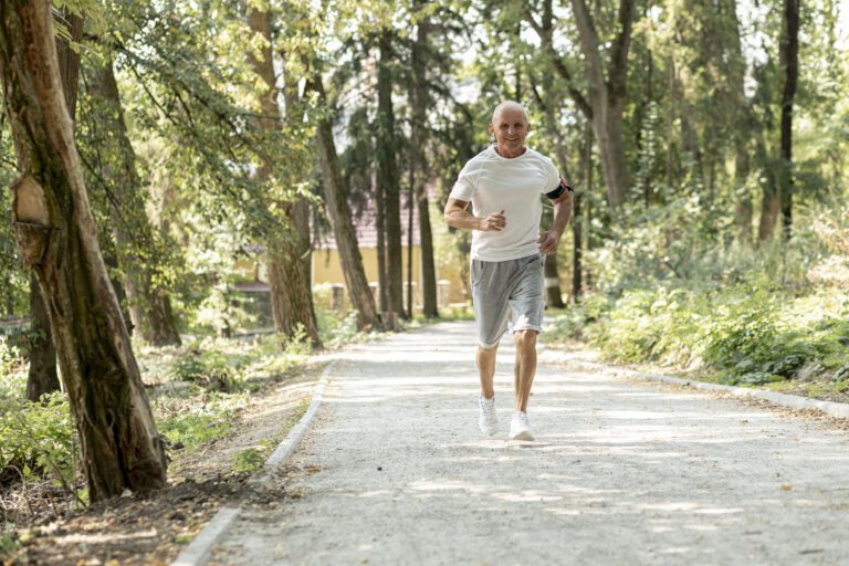 Homem sénior em forma a correr numa estrada de terra entre árvores.